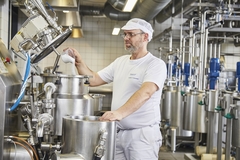Image a male factory in white tshirt and pants pouring white powder into a machine