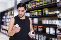 Image A man stands in a store aisle trying to choose between two different supplements.