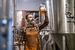 Image Bearded brewery master holding glass of beer and evaluating its visual characteristics