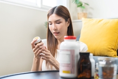 Image A beautiful person sits on a couch and examines a bottle of supplements.