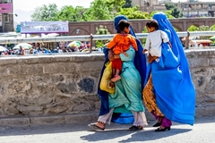 Two afghani women in burkas carry a child walking in city