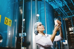 Image female scientist looking at a beaker of milk inside a factory