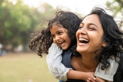 Image Mother laughs and carries her daughter on her back