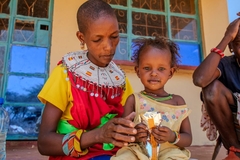 Image Sudanese mother with young daughter on her lap eating RUTF