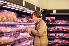 Young man looking at meat packaging label in supermarket.
