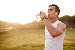 Image A man drinking a beverage in a field after a run.