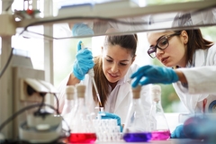 Image two female scientists working in the lab with colorful chemicals in flasks