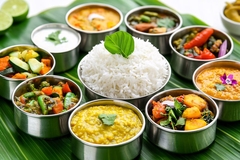 Image Diverse assortment of Indian dishes artistically arranged around a central bowl of white rice on banana leaf.