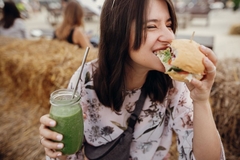 Girl enjoys a bite of burger and holds a smoothie