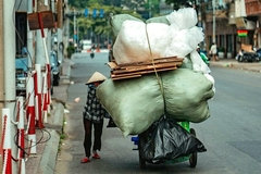 A person carrying large bags of waste on a bicycle
