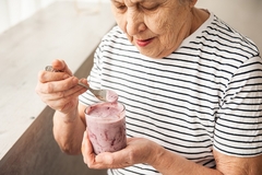 An aged woman eating yogurt.