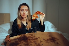 girl in bed eats leftover pizza from box