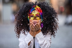 Image A woman wearing an eye mask blowing confetti toward the camera.