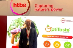 an old man in a suit standing in front of a digital signboard at a trade show