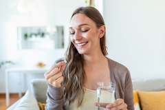 Image A woman smiles while looking at a supplement that she is holding in hand while sitting on the couch
