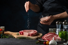Image A chef seasoning a steak with salt.