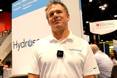 a middle aged man in a white polo tshirt standing at a trade show