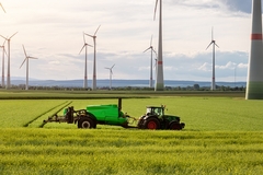 Image tractor in a huge green field with windmills in the background