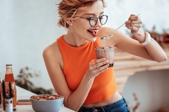 Image a young woman in an orange sleeveless top eating yogurt