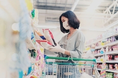 Image A person wearing a face mask and gloves in a grocery store buying things in plastic packaging