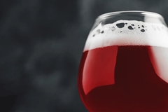 Image A close-up of a tulip glass filled with deep ruby red cherry ale, topped with a foamy head, against a dark blurred background.