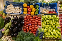 Assorted fresh vegetables including tomatoes, bell peppers, mushrooms, and eggplants displayed in crates at a local market.