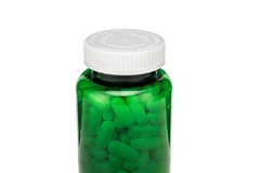 A green bottle with pills and a white cap