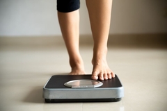 Image A woman's legs and feet with one stepping on a scale.