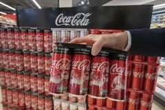Image a hand holding coca cola cans in supermarket aisle