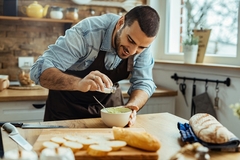 Image Young happy man seasoning food while cooking in the kitchen