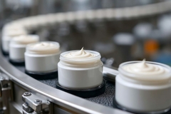 Image Pots of cream on a conveyor belt.