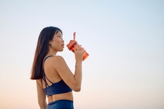Image A beautiful woman drinks a supplement in the sun after exercising.