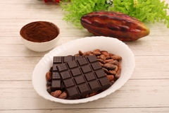 Image chocolate and cocoa beans in a white bowl with a cacao fruit in the back