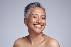 Image A woman with glowing skin smiles with her eyes closed.