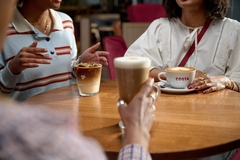 Image three friends drinking coffee in white mugs on a brown table