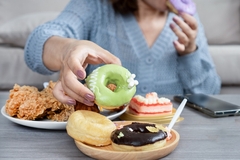 a woman reaching out for donut on a table with fried chicken and cake