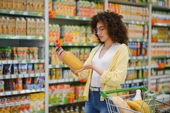 Image young woman in yellow shirt looking at yellow juice bottle in supermarket