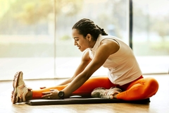 Image A woman stretches on a yoga mat in front of a large window overlooking a forest.
