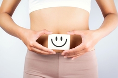 A woman hold a drawing of a smiley face over her stomach.