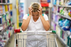 Image Upset woman holds head leaning on trolley in a supermarket