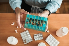 Image A hand holding a container of pills on a table full of pharma packaging