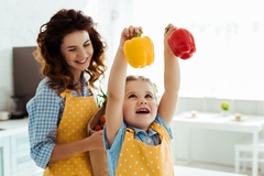 Image happy mother looking at excited daughter holding red and yellow bell peppers