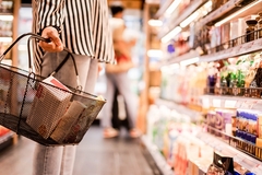 woman's hand holding a basket in supermarket food aisle