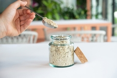 a hand holding a spoon with chicken powder and a glass jar