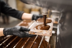 Image a hand wearing black gloves filling chocolate in mold