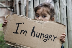 Image Little girl holding a sheet of cardboard, saying I am hungry.
