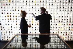 Image a man and a woman talking in front of a big wall with food ingredients on shelves