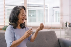 Image Close-up of a happy senior lady holding a glass of water and taking a pill.