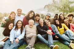 Image Many people of different ages and demographics all sitting happily in the grass at a park.