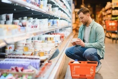 Image A man reads the nutritional information on a tub of yogurt in the dairy aisle.